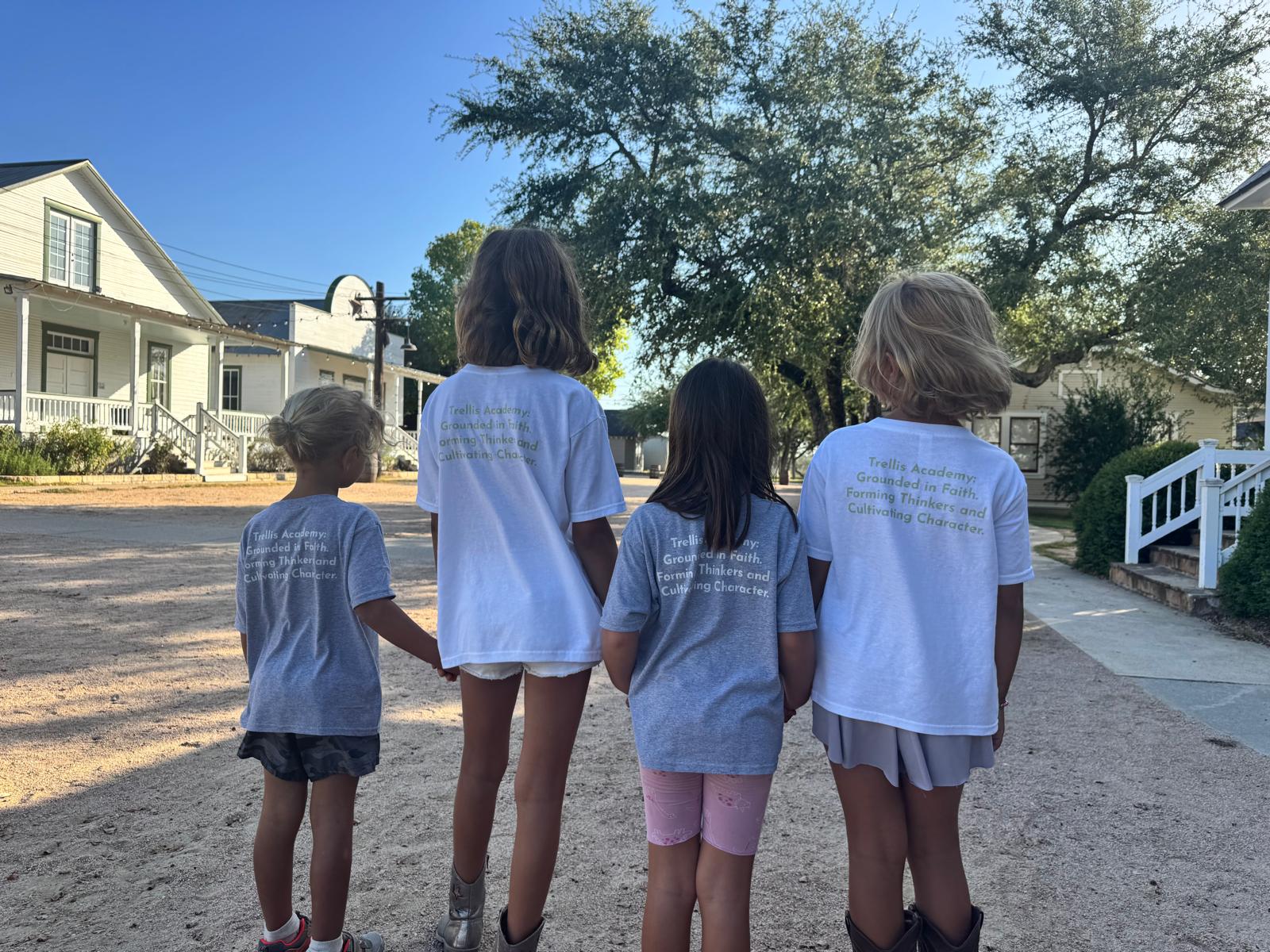 Four Trellis Academy students stand with their backs to the camera in school shirts on campus.